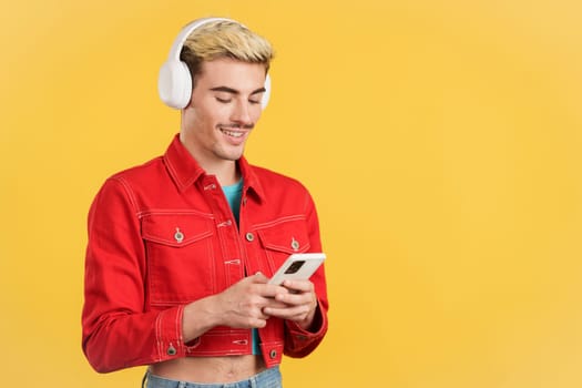 Gay man listening to music with headphones and a mobile in studio with yellow background