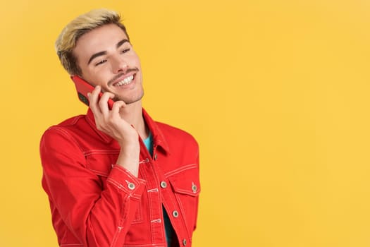 Gay man smiling while talking to the mobile phone in studio with yellow background