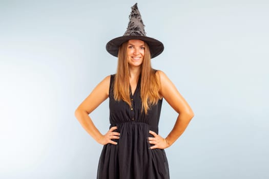 Happy Halloween. Happy brunette woman in halloween witch costume with black hat on a light background.