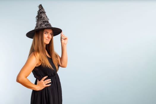 Happy Halloween. Happy brunette woman in halloween witch costume with black hat on a light background.