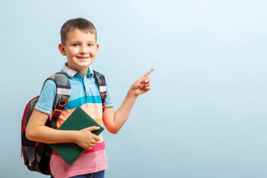 Back to school. Happy elementary school student in eyeglasses hugging book and points to an empty space on blue background. Free space.