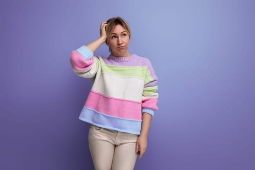 thoughtful blond young woman holding her head on purple background with copy space.