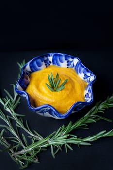 delicious pumpkin cream soup and black background with rosemary.