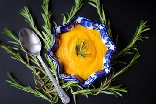 pumpkin soup on a black background with the sprigs of rosemary, close-up