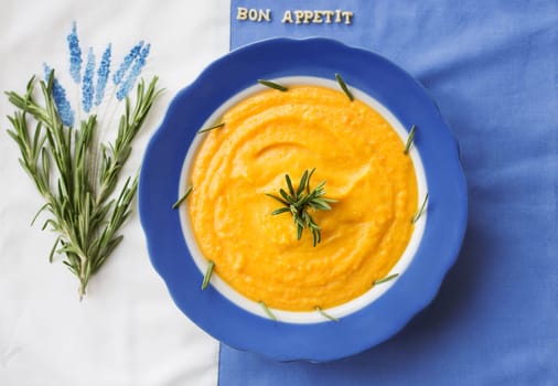 pumpkin soup in a blue plate with rosemary on a napkin with flowers.