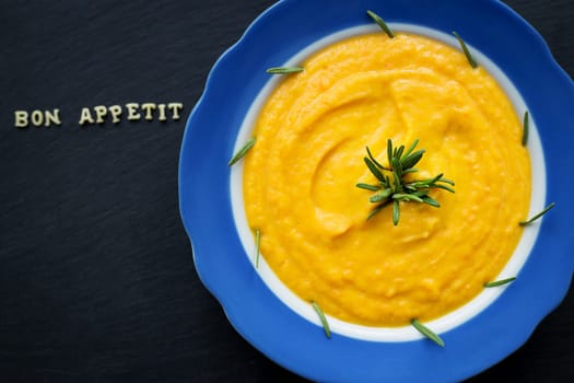 pumpkin soup in a blue plate on a black background, close-up