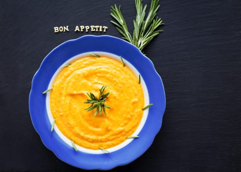 pumpkin soup in a blue plate on a black background with a sprig of rosemary