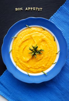 pumpkin soup in a blue plate on a black background with a blue cloth, close-up