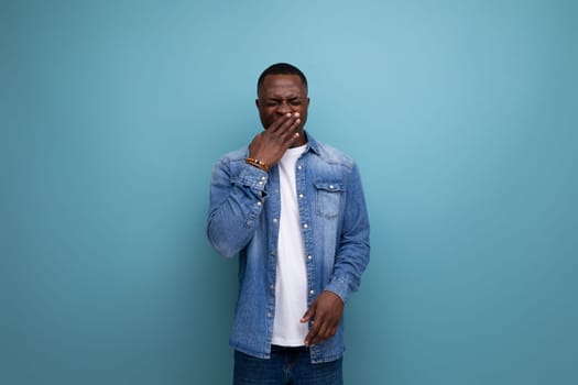 portrait of a young attractive african man dressed in stylish denim clothes covering his face with his hand.