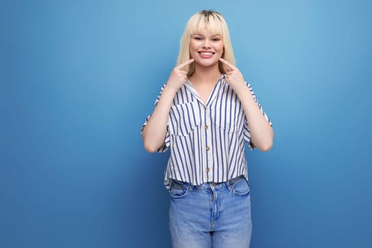 smiling blond 25 year old female person in striped blouse and jeans posing as a model.