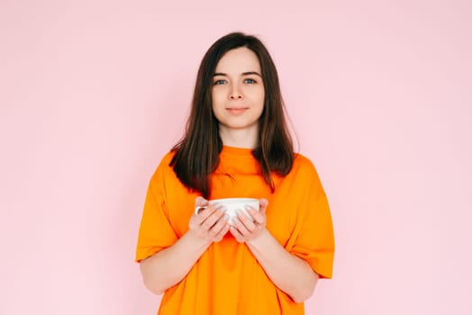 Serene Leisure: Charming Woman in Orange Attire, Savoring a Delightful Drink in a Mug - Relishing Free Time After Work, Tranquility and Bliss Isolated on Pink Background.