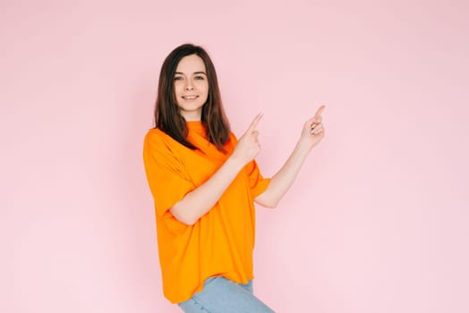 Inviting Emptiness: Cheerful Woman Pointing with Two Fingers to an Empty Space - Drawing Attention to Available Opportunities, Isolated on Pink Background.