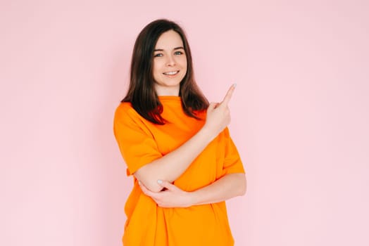 Playful Gestures: Charming Woman Pointing Finger at Empty Space - Humor and Interaction Concept, Isolated on Pink Background