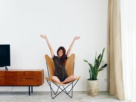 Woman sitting in a leather armchair near the window hands up smile , modern stylish interior Scandinavian lifestyle, copy space. High quality photo