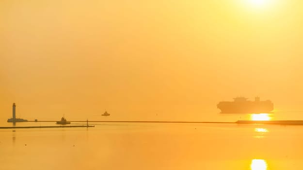 Container ship arrives a port during beautiful sunset. The ship sails to the lighthouse.