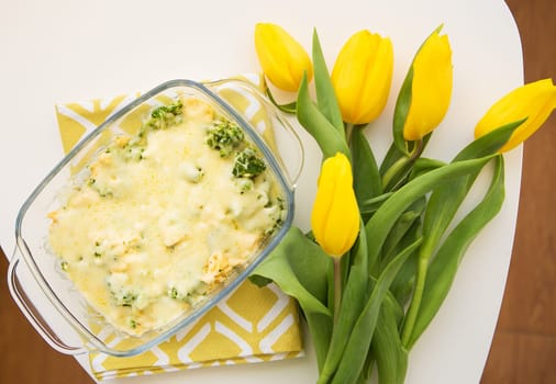 tasty casserole with broccoli, cheese and cream on a background of yellow tulips