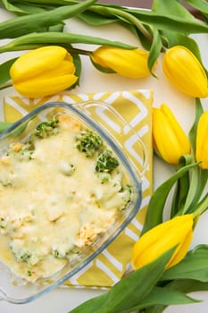 tasty casserole with broccoli, cheese and cream on a background of yellow tulips, close-up