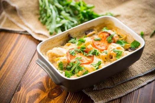 cauliflower baked with chicken fillet and mushrooms under cheese in a ceramic form, on a wooden table.