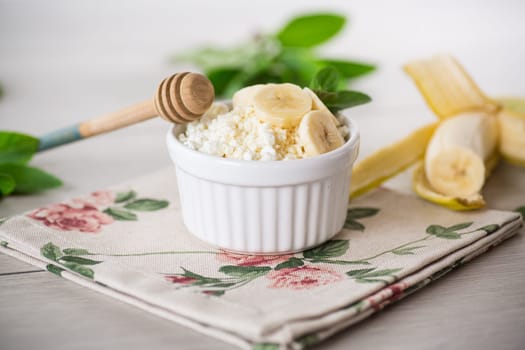 crumbly organic cottage cheese with honey and bananas in a ceramic bowl on the table