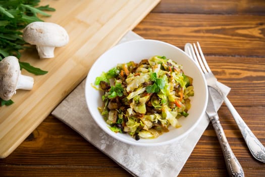 cabbage early fried with mushrooms, carrots and vegetables in a white bowl on a wooden table