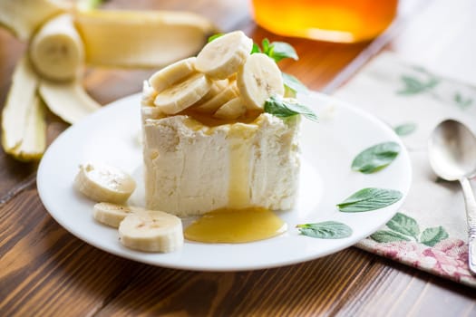 Portion of homemade milk curd with banana slices and honey, with mint in a plate.
