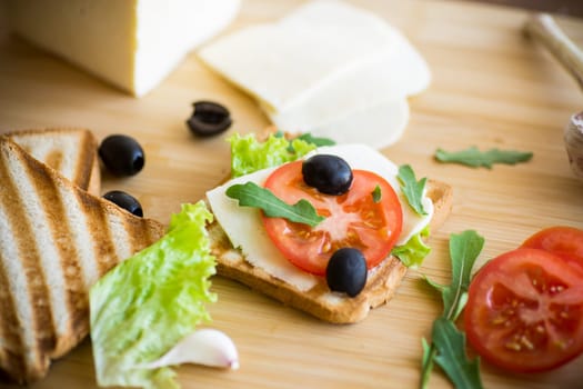 fried toasts with mozzarella, lettuce and tomatoes with herbs on a wooden table