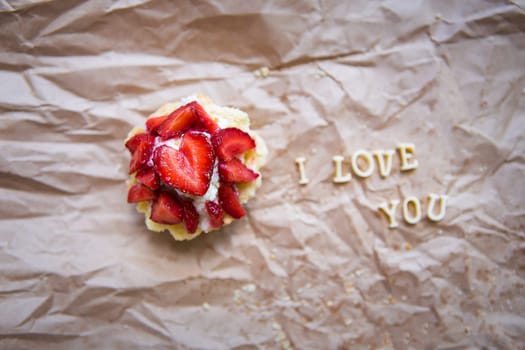 Bright cupcake with strawberries lies on craft paper, the inscription I love you. valentine card