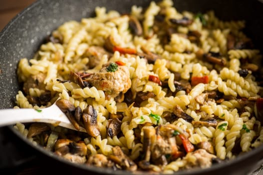 vermicelli cooked with mushrooms, meat and vegetables in a frying pan on a wooden table