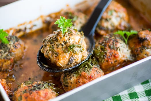 cooked meatballs from minced meat in a sauce in a ceramic form, on a wooden table