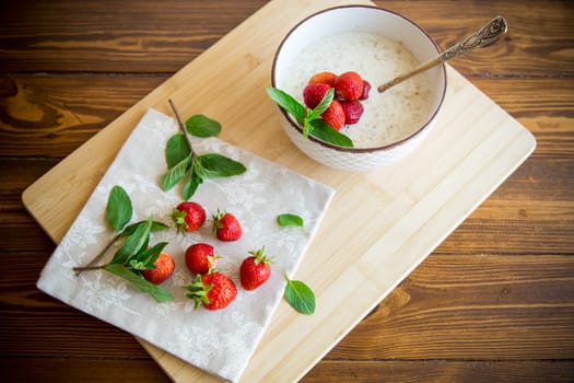 cooked diet oatmeal in a bowl with fresh ripe strawberries, on a wooden table.