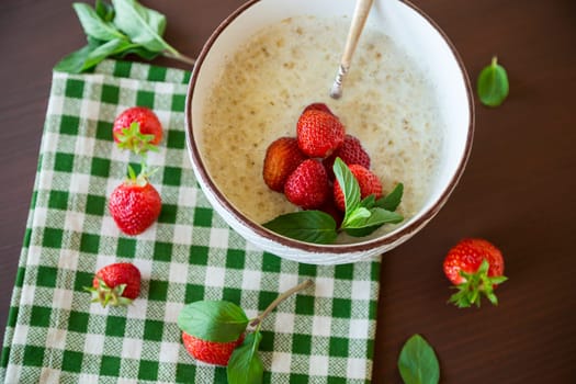 cooked diet oatmeal in a bowl with fresh ripe strawberries, on a wooden table.