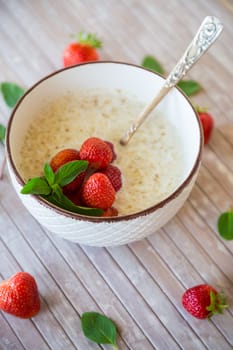 cooked diet oatmeal in a bowl with fresh ripe strawberries, on a wooden table.