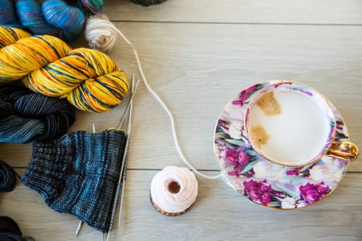 Colored threads, knitting needles and other items for hand knitting, on a light wooden table .