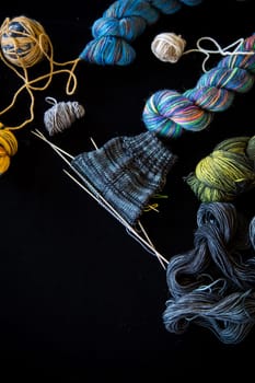 Colored threads, knitting needles and other items for hand knitting, on a black background .