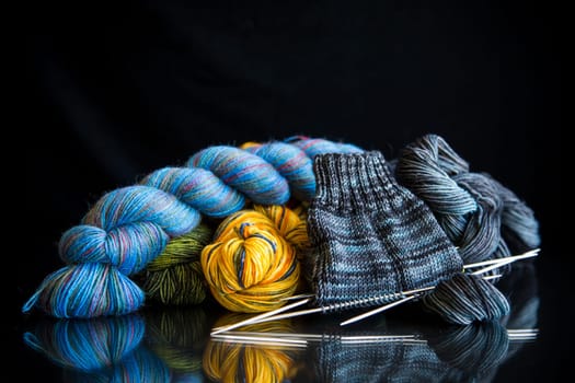 Colored threads, knitting needles and other items for hand knitting, on a black background .