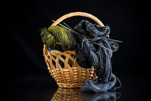 Colored threads, knitting needles and other items for hand knitting, on a black background .