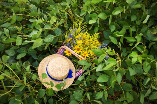 straw hat and basket with flowers stand on the grass.