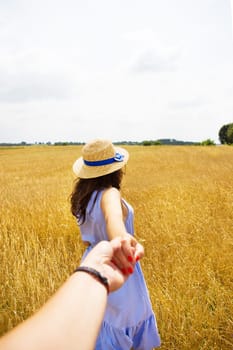 a girl in a blue dress is standing with her back in a wheat field.