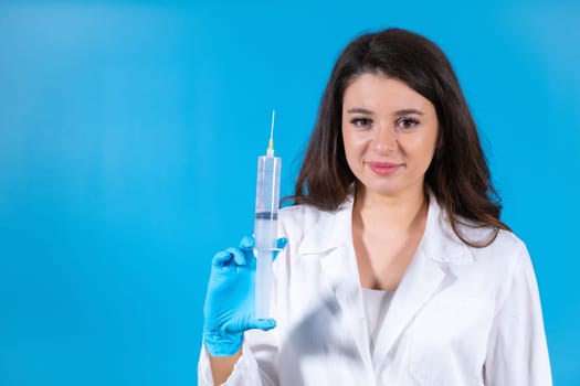 Woman nurse prepares syringe to vaccinate sick patient at blue hospital wall. Brown-haired lady doctor in hospital robe treats patient at appointment