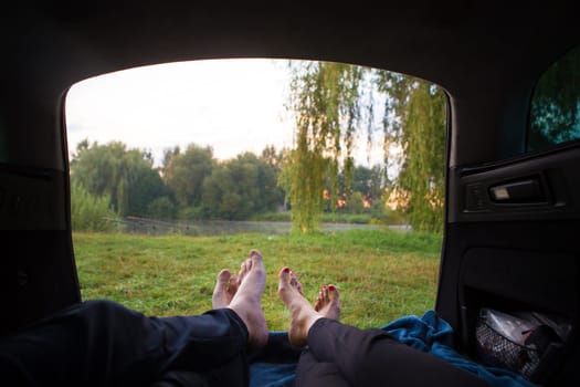 Man and woman relaxing in the trunk of a car near a lake.