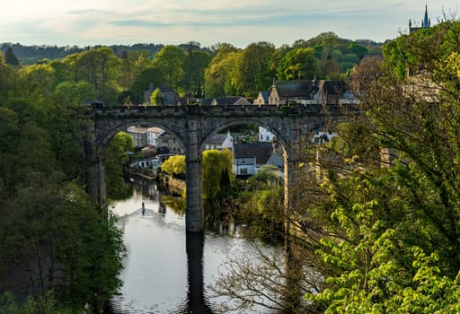 Stone viaduct over River Nidd at Knaresborough with lone paddleboard on the calm surface