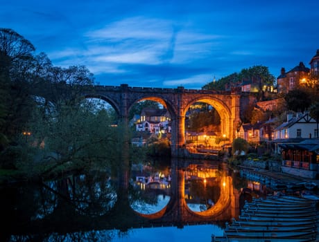 Stone viaduct over River Nidd at Knaresborough with rowing boats by riverbank at night