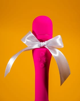 Pink vibrator with a white bow on an orange background. Women's gift