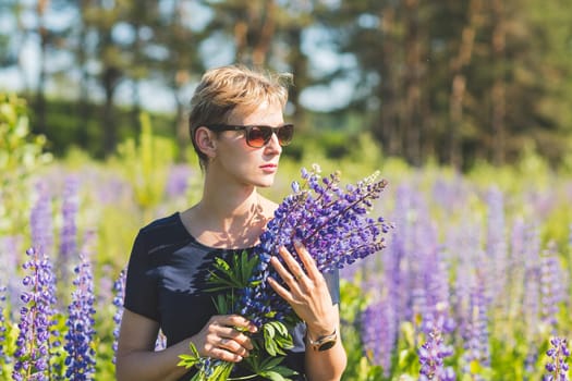 Portrait of young woman holding bouquet of lupin flowers walking in summer meadow.