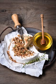 Camembert soft cheese is served on an iron dish with walnuts, honey and thyme. 