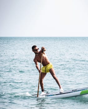 a sporty guy swims on a sup board with a paddle on the sea during the day against a beautiful sky in summer