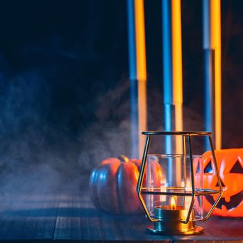 Halloween holiday concept design of pumpkin, candle, spooky decorations with blue tone smoke around on a dark wooden table, close up shot.