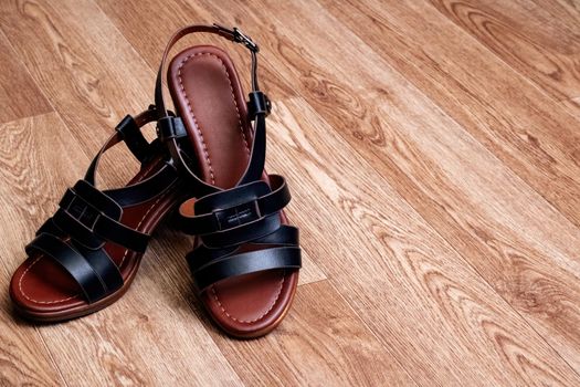 Women's black sandals with straps on woodenbackground close up, copy space