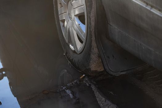 Black car wheel stuck in mud close up