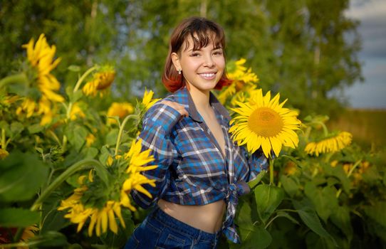 Smiling young woman among blooming sunflowers in a field